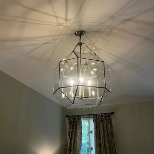 A geometric glass chandelier casts intricate shadows on the ceiling, illuminating a softly decorated room.