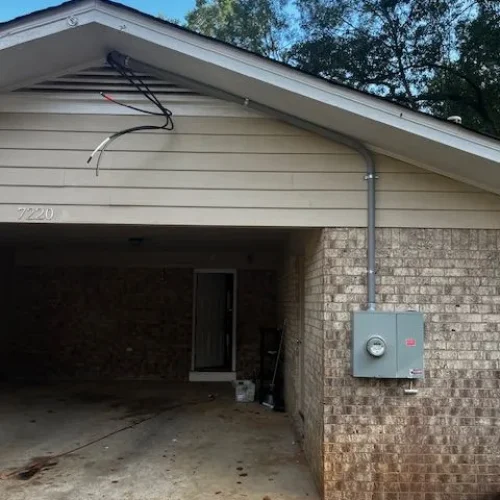 A residential garage with a sloped roof, featuring exposed wiring, a gray electric meter box, and a concrete driveway.